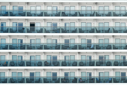 View of a cruise ship's exterior, showcasing rows of balconies with chairs and tables, reflecting a serene ocean voyage, Willemstad, Curacao.