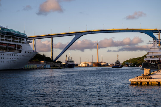 View of a majestic bridge arches over the shimmering waters, connecting vibrant shores lined with ships, creating a captivating contrast of industry and beauty, Willemstad, Curacao.