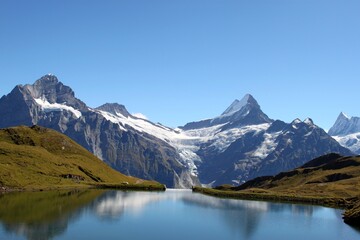 Fototapeta premium Bachalpsee lake reflecting alpine peaks near Grindelwald, showcasing pristine nature, clear water, and dramatic mountain scenery.
