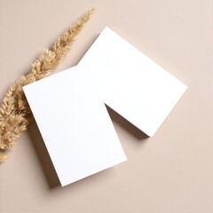 Two blank, textured cards lie side by side on a rustic wooden surface, adorned with a delicate wheat plant, showcasing its golden stalks and feathery grains.