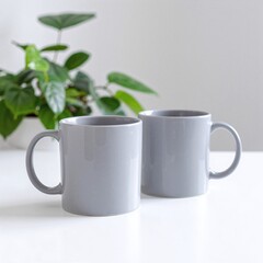 Two elegant gray ceramic mugs with smooth finishes rest side by side on a pristine white table, casting soft shadows in the warm light.