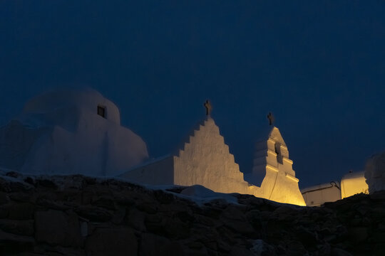 View of the stark white, cubist architecture of the Holy Church of Panagia Paraportiani glows against the deep blue twilight sky, Mykonos, Greece.