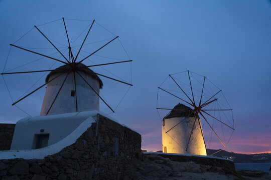 View of iconic white windmills standing majestically against the deep twilight sky, their sails poised above stone bases, Mykonos, Mykonos, Greece.