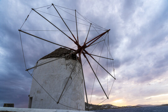 View of the iconic whitewashed windmill stands silhouetted against a dramatic sky painted with hues of twilight in the Aegean Sea, Mykonos, Mykonos, Greece.