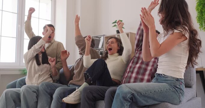 Fans group watching soccer match together on TV at home. Young friends cheering and sitting on sofa in living room, clapping and shouting, celebrating goal, victory of team with laughter and energy