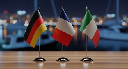 German, French, and Italian flags on a table with a blurred harbor background at night