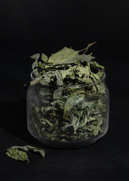 Dried mint in a glass jar on a black background.