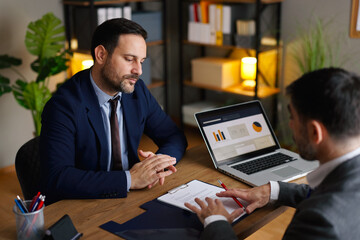 Businessmen analyzing a contract document and discussing terms at an office desk