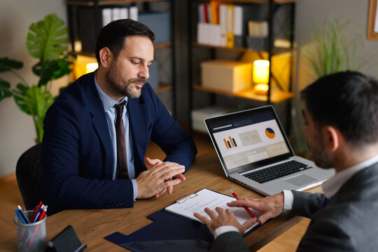 Businessmen analyzing a contract document and discussing terms at an office desk