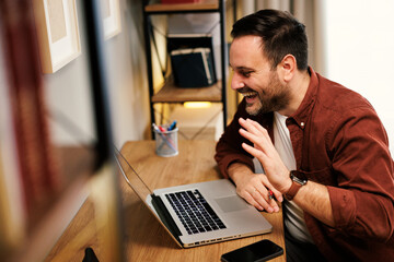 Happy man waving during a video conference call on laptop, working from home