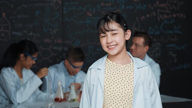Asian scientist show miniheart to camera while diverse group doing experiment. Young schoolgirl standing at blackboard with chemical theory written while wearing lab coat at laboratory. Edification