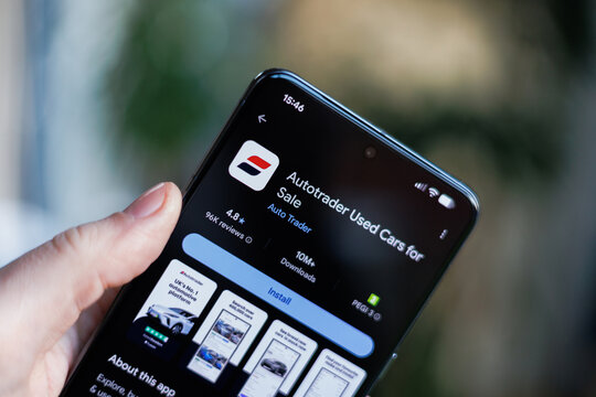 Phone in hand displaying Autotrader Used Cars for Sale app on Google Play Store