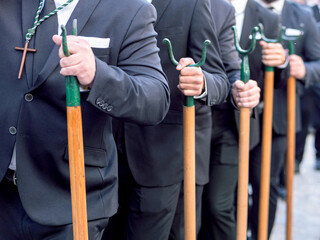 Men in black suits carrying traditional metal staffs during a religious procession