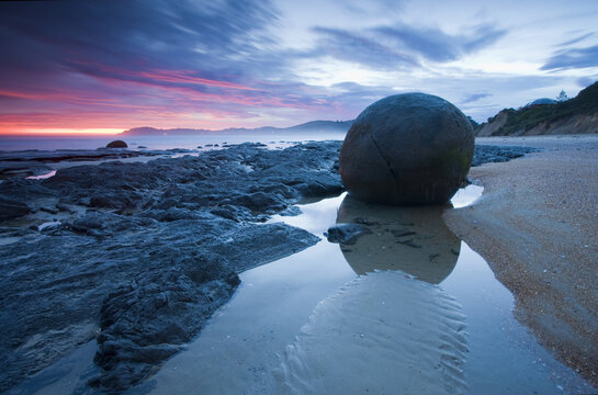 View of spherical boulders scattered across the beach reflecting the vibrant twilight sky in the wet sand, Hampden, Otago Region, New Zealand.