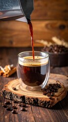 Dark coffee being poured into a glass on a wooden coaster, surrounded by beans and spices, on a wooden table
