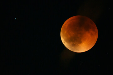 A high-magnification view of a total lunar eclipse, showing the Moon fully within the Earth's umbral shadow and displaying the reddish color caused by Rayleigh scattering of sunlight through the Earth