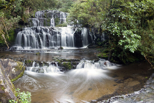 View of water cascading down rocky steps, embraced by verdant foliage, creating a serene symphony of nature's beauty, Purakaunui, Otago Region, New Zealand.