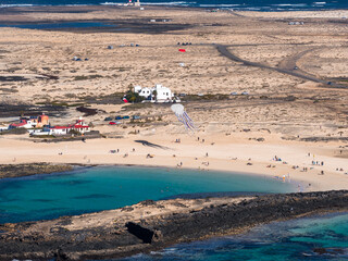 Aerial turquoise cove by volcanic rock and dunes in Fuerteventura, Canary Islands. Beachgoers relax as a jellyfish kite casts a shadow. Midday light and clear surf. © Aerial Film Studio