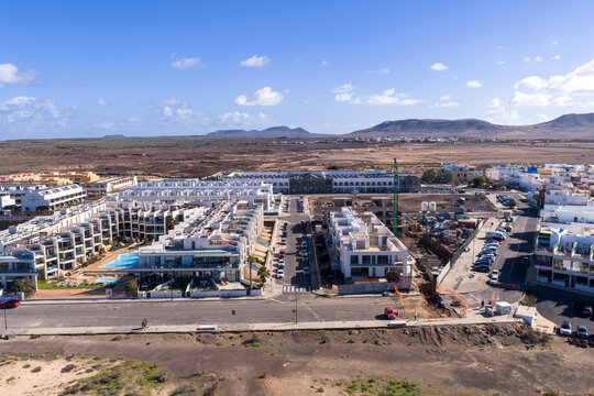 Aerial view of Fuerteventura, Canary Islands, with white villas, a green crane, pools, and a promenade near Playa del Bajo de la Burra under clear midday light.