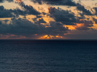 Stormy clouds break at sunset off Fuerteventura, Canary Islands, as golden sunbeams strike the Atlantic. Deep blue ocean meets orange and violet sky in cinematic light.