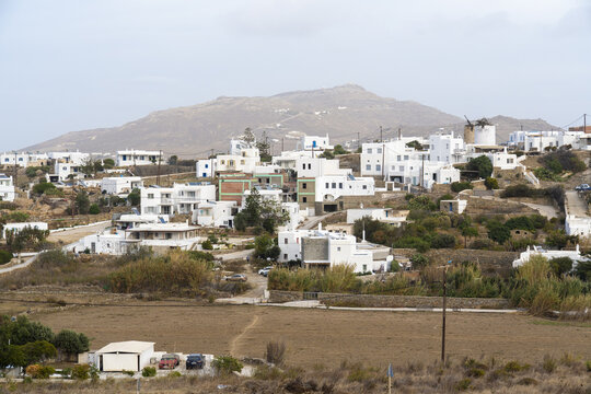 View of whitewashed houses and windmills nestled against a rugged hillside, bathed in soft light, creating a timeless scene of Greek architecture, Ano Mera, Mykonos, Greece.