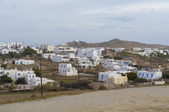 View of whitewashed buildings with blue accents cascade down the sun-drenched hills under a muted sky, capturing the essence of island life, Ano Mera, Mykonos, Greece.