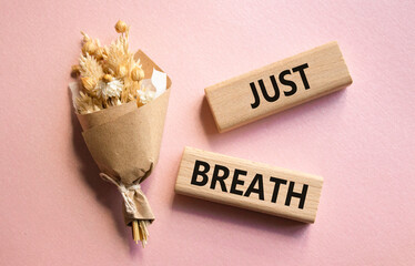 Just Breathe symbol. Wooden blocks with words Just Breathe. Beautiful pink background with bouquet of flowers. Business and Just Breathe concept. Copy space.