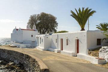 View of whitewashed buildings shimmering under the bright sun along the coastline, with a charming church standing proudly, Mykonos, Greece.