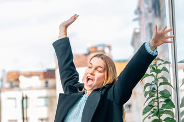 a young woman raises her arms with an expression of happiness and enthusiasm outdoors
