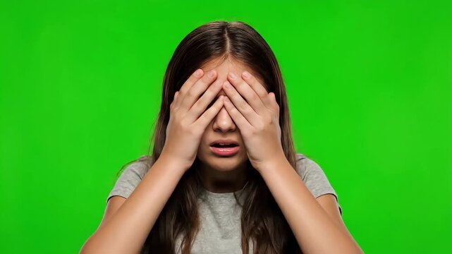 Young woman covering face with hands expressing shock or surprise on green background