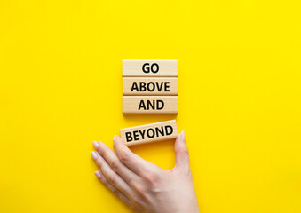 Go above and beyond symbol. Concept words Go above and beyond on wooden blocks. Beautiful bright yellow background. Businessman hand. Business and Go above and beyond concept. Copy space.