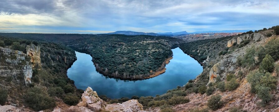 Expansive panoramic vista of the famous Curvas del Duero viewpoint, showcasing the river's impressive meander through the Soria landscape under a vast, textured sky in Castilla y Le&oacute;n, Spain.