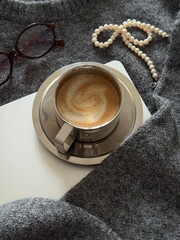 Cozy Gray Sweater laptop Coffee Glasses. Soft Knit Texture, Ceramic Latte With Foam Art Resting On Paper Journal, Folded Wool Blanket, Reading Glasses Nearby, Neutral Palette,
