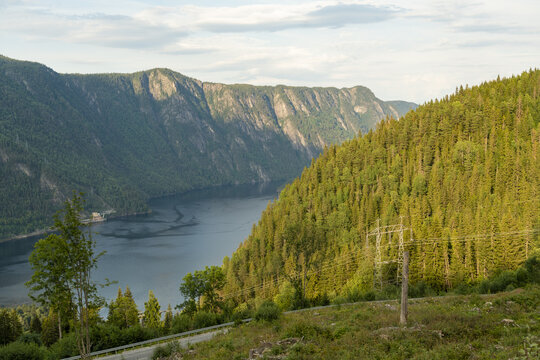 View of the serene, dark waters of a fjord nestled between towering, verdant mountainsides under a soft sky, Dalen, Telemark, Norway.