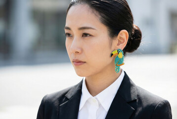 Asian woman wearing colorful earrings and looking thoughtful outdoors  