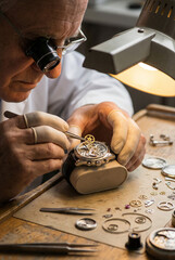 Elderly man repairing watch with tools on workbench in workshop  