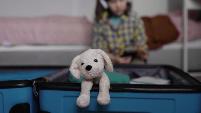 Child packs suitcase for travel with a stuffed toy dog.