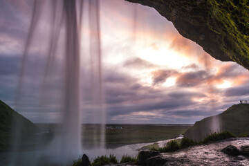 View of powerful Seljalandsfoss waterfall cascading down, contrasted against the expansive sky and rugged landscape, South Island, Iceland.
