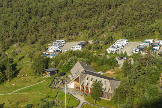 View of a modern building nestled amidst lush green trees, with campers parked nearby under the clear sky, a tranquil scene, Preikestolen, Rogaland, Norway.