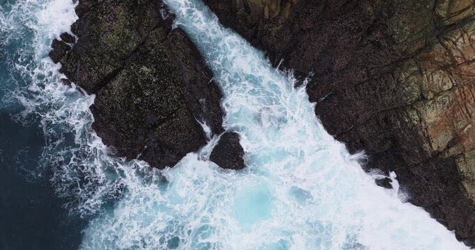 Top down aerial of Atlantic waves surging through a narrow rocky channel near Coruna, Galicia, Spain, powerful surf and white foam patterns