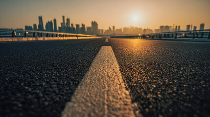 Low angle view of an empty road leading towards a modern city skyline during golden hour with warm sunlight reflecting on the asphalt surface