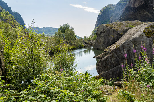 View of a tranquil river reflecting the sky, nestled between rugged cliffs and verdant foliage, creating a serene landscape, Helleren, Jossingfjord, Norway.