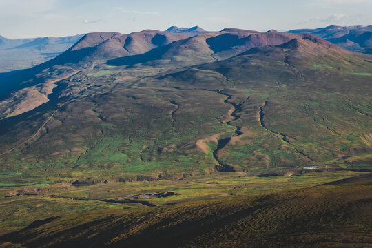 View of rolling hills covered with patches of green and brown vegetation under a blue sky in Tindastoll mountain, Saudarkrokur, Skagafjordur, Iceland.