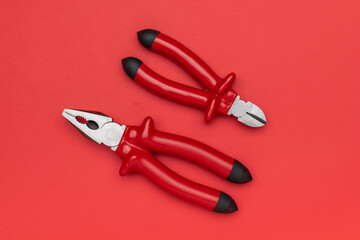 Obraz premium Top View of Pliers and Wire Cutters on Vibrant Red Background