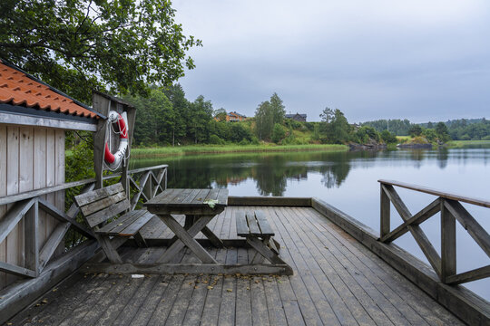 View of the calm lake reflecting the sky from a wooden deck with benches and a life preserver hanging on a wall, Treungen, Telemark, Norway.