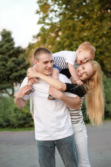 Happy family is playing cheerfully in the park in the summer. Father holding kid on shoulders.