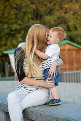 Mom and son outdoors in the summer. Mother is hugging the kid boy and kissing him