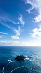 Small island sits in a vast, bright blue ocean under a partly cloudy sky. Sunlight reflecting on the water