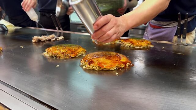 A chef at a local Japanese restaurant prepares okonomiyaki, seasoning it with spices. It's a popular dish in Hiroshima: pancake batter cooked with various fresh ingredients on a hot steel griddle.