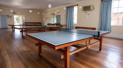Large room in an old community center features tables set up for dinner, a table tennis area, and bright lighting throughout the space